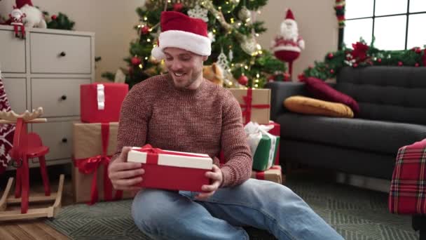 Νεαρός Καυκάσιος Άνδρας Ξεπακετάρει Δώρο Κάθεται Δίπλα Στο Χριστουγεννιάτικο Δέντρο — Αρχείο Βίντεο