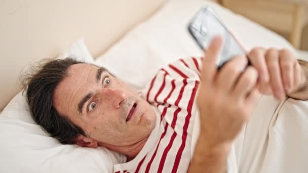 Μεσήλικας Άντρας Που Χρησιμοποιεί Smartphone Ξαπλωμένος Στο Κρεβάτι Έκπληκτος Στο — Αρχείο Βίντεο