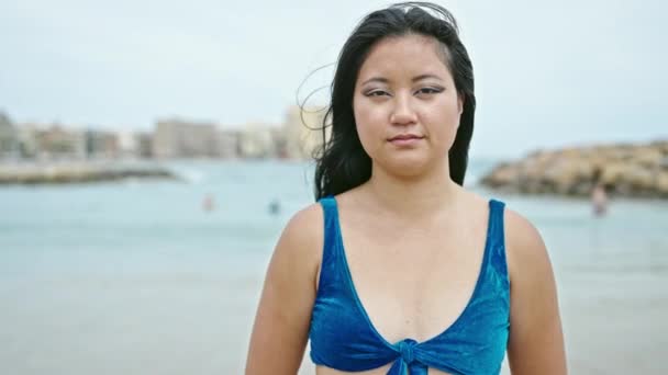 ビーチで深刻な顔で立っているビキニを身に着けている若い中国人女性観光客 — ストック動画