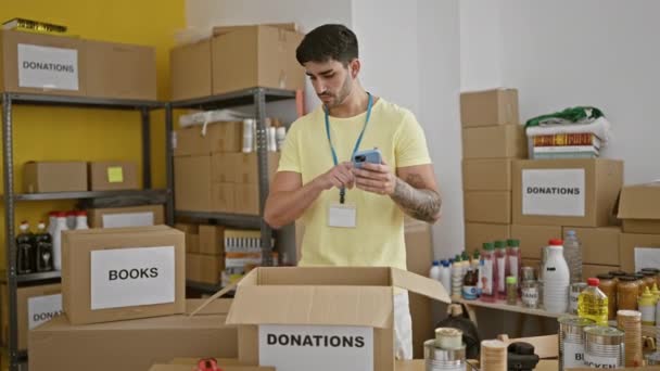 Ung Latinamerikansk Man Volontär Med Hjälp Smartphone Kontrollera Produkter Välgörenhetscenter — Stockvideo