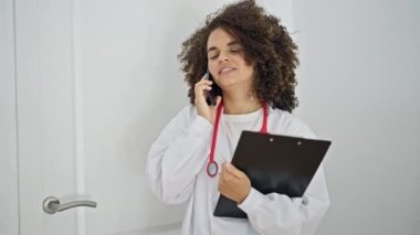 Genç, güzel İspanyol kadın doktor. Akıllı telefondan konuşuyor. Kliniğin kapısından içeri giriyor.
