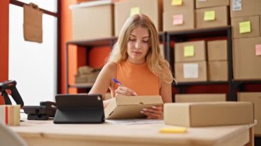 Genç sarışın kadın ecommerce iş işçisi. Ofisteki pakette dokunmatik kağıt kullanıyor.