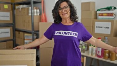 Orta yaşlı İspanyol kadın gönüllü üniformasını göstererek hayır kurumuna gülümsüyor.