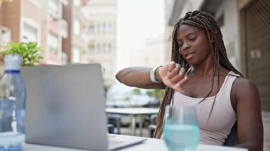 Laptop kullanan Afrikalı Amerikalı bir kadın kahve dükkanının terasında nöbet tutuyor.