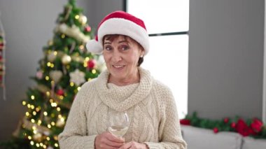 Olgun İspanyol kadın kameraya konuşuyor. Evde Noel ağacının yanında şarap içiyor.