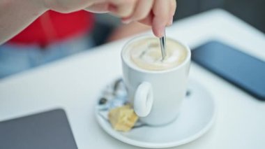 Kahve dükkanının terasında oturan genç sarışın kadın kahveyi karıştırıyor.