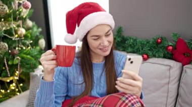 Kafkasyalı genç bir kadın Noel 'i akıllı telefonla kutluyor evde kahve içiyor.