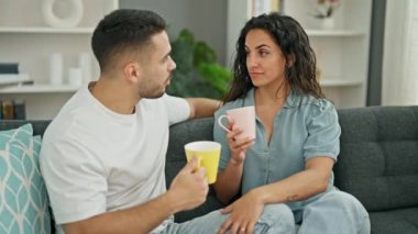 Kanepede oturan erkek ve kadın çift evde kahve içip öpüşüyorlar.