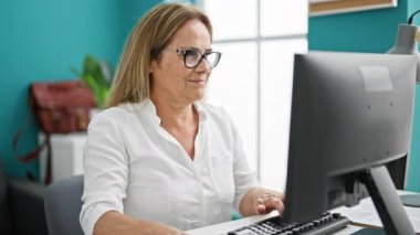 Orta yaşlı İspanyol iş kadını ofiste bilgisayar kullanıyor.
