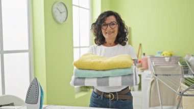 Orta yaşlı İspanyol kadın çamaşır odasında katlanmış havluları tutarken kendine güler.