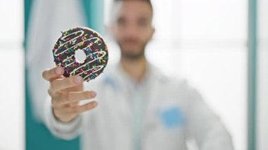 Genç İspanyol doktor masada oturmuş, elinde donutla klinikte parmağıyla hayır diyor.