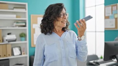 Orta yaşlı İspanyol iş kadını. Ofiste çalışan akıllı telefondan sesli mesaj gönderiyor.