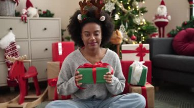 Ren geyiği kulağı takan Afrikalı Amerikalı bir kadın Noel hediyesini evde tutuyor.