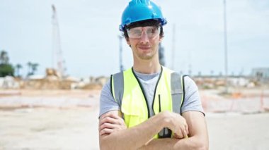 Kollarını kavuşturmuş genç İspanyol mimar inşaat alanında baş parmak hareketi yapıyor.