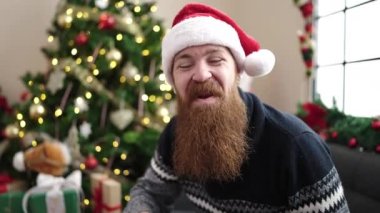 Genç kızıl saçlı adam Noel ağacının yanında oturmuş evde öpüşüyor.