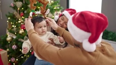 Ren geyiği kulağı takan çift ve oğul evdeki Noel ağacının yanında kanepede oturuyorlar.