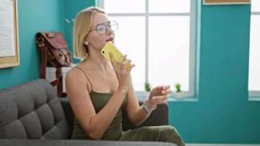 Genç sarışın iş kadını akıllı telefondan konuşuyor ofiste gülümsüyor.