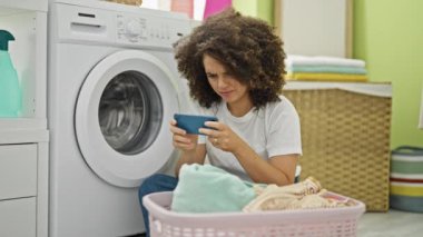 Çamaşır odasında video oyunu oynayan genç, güzel İspanyol kadın çamaşır makinesini bekliyor.