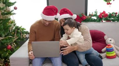 Çift ve oğlu evdeki Noel ağacının yanında dizüstü bilgisayar kullanıyor.