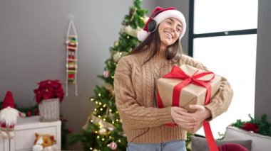 Genç, güzel, İspanyol bir kadın elinde Noel hediyesiyle evde müzik dinliyor ve dans ediyor.
