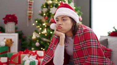 Genç, güzel, İspanyol bir kadın Noel ağacının yanında, koltukta oturmuş, üzgün üzgün üzgün eve bakıyor.