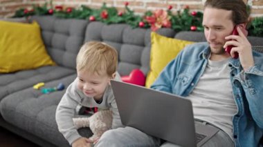 Baba oğul Noel 'i evde dizüstü bilgisayarla oyuncaklarla oynayarak kutluyorlar.