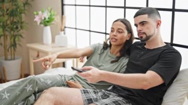 Güzel bir çift, rahat bir yatakta uzanıyor, sinemadan zevk alıyor, rahatlatıcı bir yatak odasında neşeyle gülümsüyor.