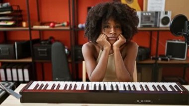 Müzik stüdyosunda üzgün bir ifadeyle masada oturan Afrikalı Amerikalı kadın müzisyen.