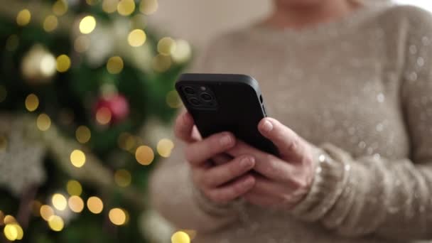 Midaldrende Kvinde Med Gråt Hår Ved Hjælp Smartphone Ved Juletræ – Stock-video
