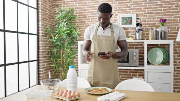 Afrikanischer Mann Kocht Kekse Und Sucht Online Rezept Auf Smartphone — Stockvideo