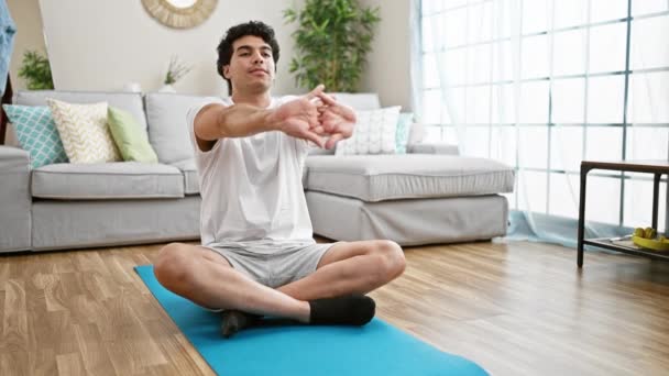 年轻的拉丁男子坐在地板上 练习瑜伽 在家里伸展身体和胳膊 — 图库视频影像