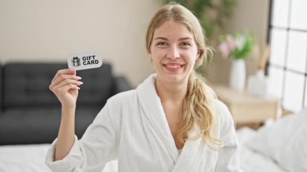 Young Blonde Woman Wearing Bathrobe Sitting Bed Pointing Gift Card — Stock Video