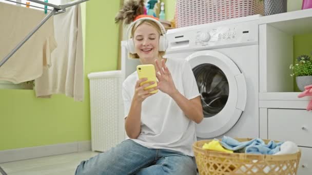 Ung Blond Kvinna Med Smartphone Och Hörlurar Ler Mot Tvättstuga — Stockvideo