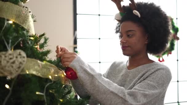 自宅でクリスマスツリーを飾るトナカイの耳を着ているアフリカ系アメリカ人女性 — ストック動画