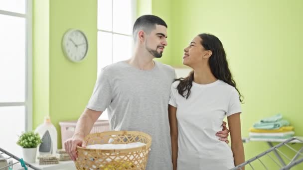 在舒适的家中 一对年轻漂亮的夫妇在洗衣房里抱着满满一篮子衣服 享受着一起洗衣服的乐趣 拥抱在一起 — 图库视频影像