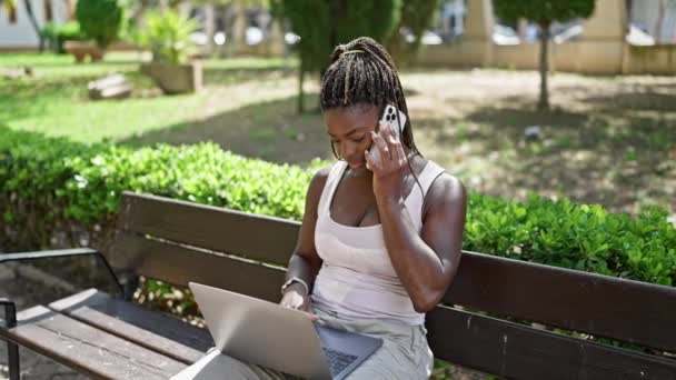 Afroamerikansk Kvinna Talar Smartphone Med Bärbar Dator Sitter Bänk Parken — Stockvideo