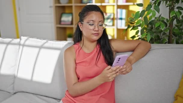 Young Chinese Woman Using Smartphone Sitting Sofa Home — Video