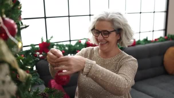 自宅でクリスマスツリーを飾る自信を持って笑顔の灰色の髪を持つ中年の女性 — ストック動画
