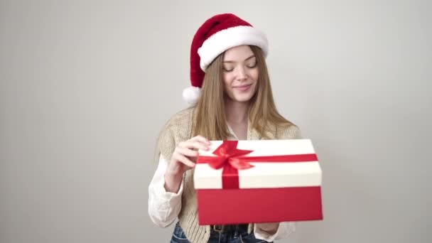 クリスマスの帽子を身に着けている若い金髪の女性は 孤立した白い背景上の贈り物を荷を解く — ストック動画