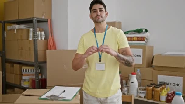 Joven Hispano Voluntario Sonriendo Confiado Haciendo Gesto Corazón Centro Caridad — Vídeo de stock