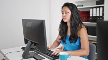 Genç Çinli iş kadını bilgisayarla ofiste kahve içiyor.