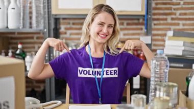 Masada oturan genç sarışın kadın gönüllü olarak hayır kurumunda üniforma giymeyi işaret ediyor.