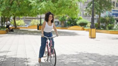 Parkta bisiklet sürerken gülümseyen güzel bir İspanyol kadın.