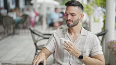 Genç İspanyol adam akıllı telefonda konuşuyor. Kahve dükkanının terasında kahve içiyor.