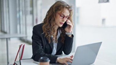 Genç bir iş kadını bilgisayarla ofiste akıllı telefondan konuşuyor.
