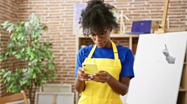African american woman artist using smartphone standing at art studio