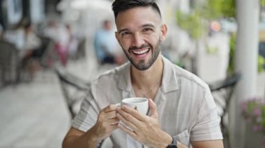 Genç İspanyol gülen adam kahvecinin terasında kendinden emin bir şekilde kahve içiyor.