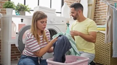 Man and woman couple smiling confident washing clothes at laundry room