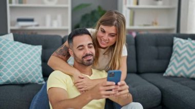 Man and woman couple using smartphone sitting on sofa at home