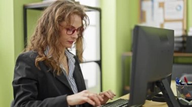 Ofiste gülümseyen bilgisayar kullanan genç bir iş kadını.